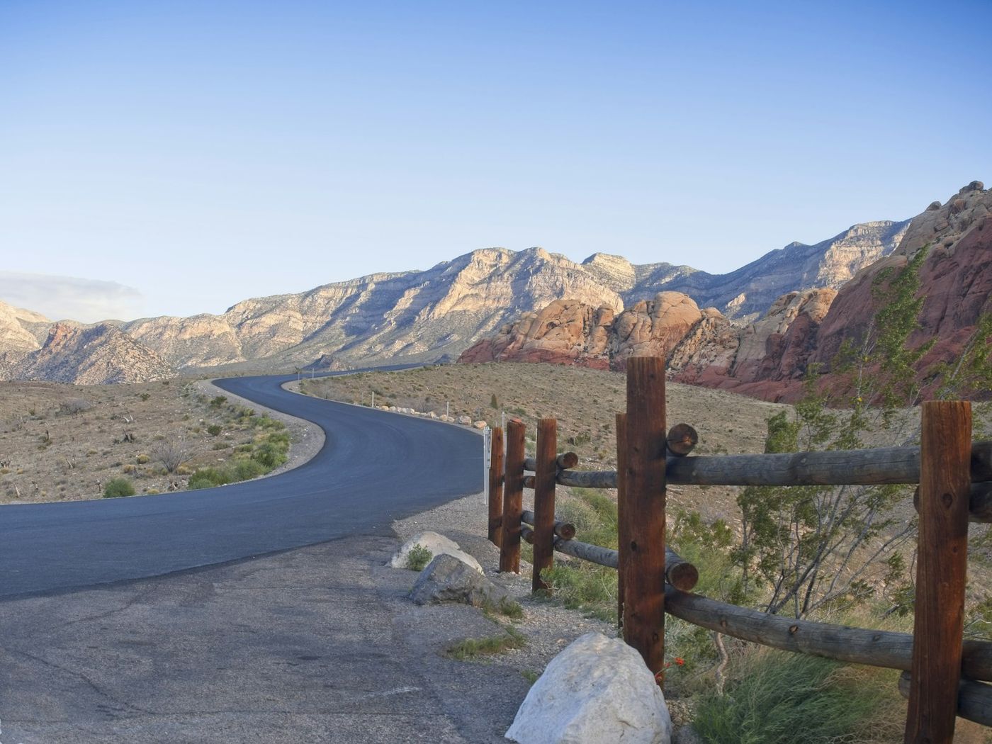 The scenic drive curving through Red Rock Canyon beside a split-rail fence
